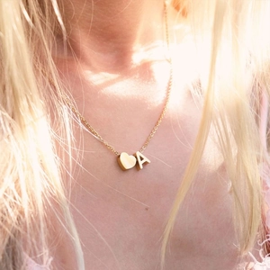 Primo piano di una collana dorata con pendenti a cuore e lettera A indossata da una donna
