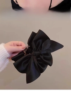 Dettaglio di un grande fermaglio per capelli a fiocco in raso nero con trama lucida