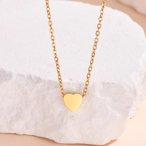 Macro detail of a golden heart pendant necklace hanging on a white textured mineral stone