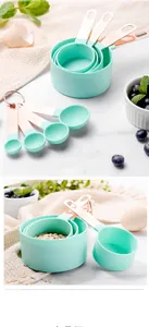 Close-up of mint green measuring cups with rose gold handles on white marble surface
