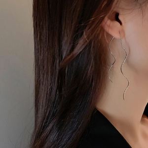 Detail of silver wavy tassel drop earrings worn on a model's ear for an elegant look