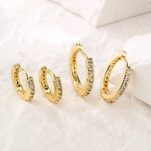 Minimalist gold hoop earrings with sparkling zircon inlay displayed on a textured stone base