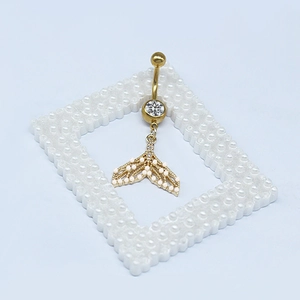 Dettaglio del piercing all'ombelico dorato con pendente a coda di sirena e perle eleganti
