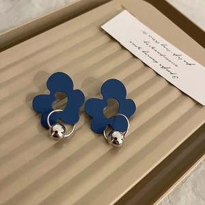 Close-up of matte blue flower earrings with silver sphere charms on beige tray