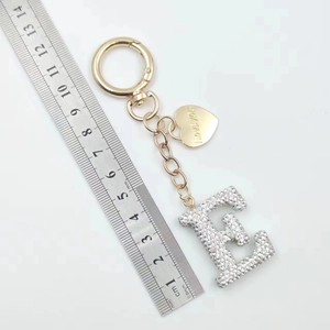 Golden letter E keychain with rhinestones and heart charm next to a measuring scale