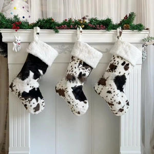 Detailed view of three plush cow print Christmas stockings with white faux fur trim on mantle