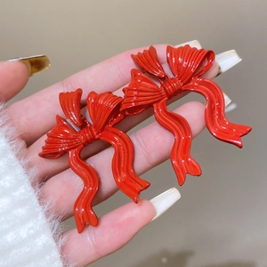 Detailed view of glossy red bow earrings held in hand against white plush background