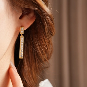 Détail de boucles d'oreilles pendantes dorées avec zircons portées par un mannequin