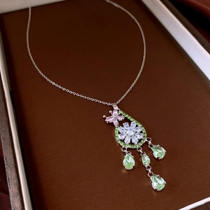 Détail macro d'un pendentif fleur argenté avec gemmes vertes et touches roses en écrin