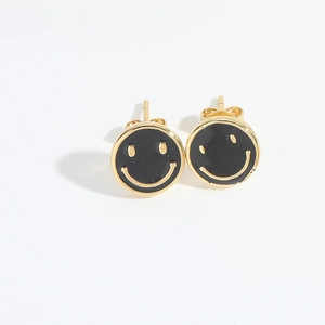 Detail of golden stud earrings featuring black enamel smiley face designs on white background