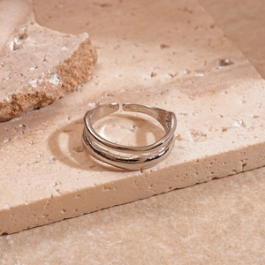 Close-up of double-layered silver geometric open ring on a textured beige stone base