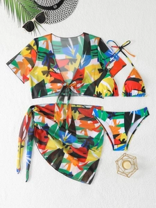 Dettaglio di un set bikini quattro pezzi con stampa tropicale, cardigan in rete e pareo su sabbia