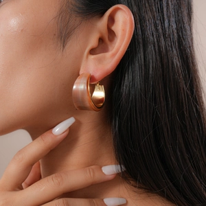 Close-up of wide C-shape resin hoop earring with peach marble pattern on model