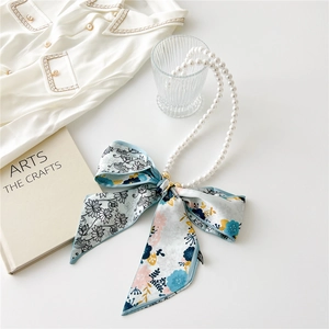 Close-up of elegant pearl chain and blue floral silk ribbon bow as bag accessory