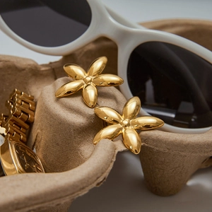 Luxury gold flower earrings with polished metal finish shown next to sunglasses