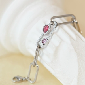 Détail d'un bracelet trombone argenté avec pierre rouge en forme de poire et zircon rose