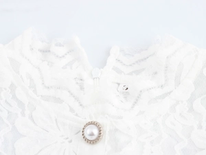 Détail de l'encolure en dentelle blanche avec boutons perlés et fermeture éclair