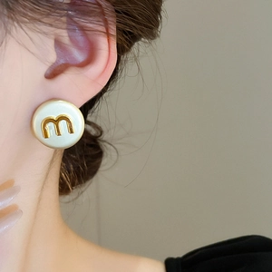 Close-up of minimalist round cream earring with golden 'm' letter on model ear
