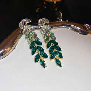 Gros plan de boucles d'oreilles feuilles en strass vert émeraude avec franges et base dorée