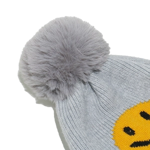 Close-up of gray knit beanie with fluffy faux fur pompom and yellow smiley face patch