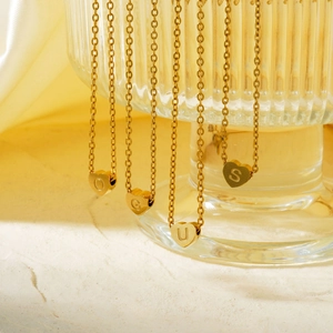 Elegant gold heart initial pendant necklace collection hanging on fluted glass display