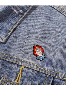 Detail of praying hands with flame enamel pin badge attached to blue denim jacket fabric