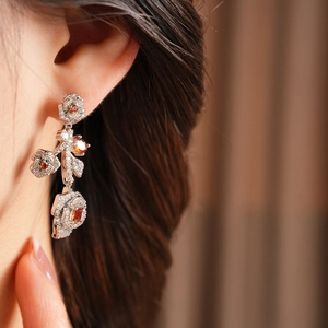 Close-up of vintage flower drop earrings with orange stones and zircon inlays on a model