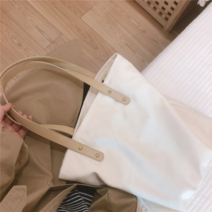 Detail of white canvas tote featuring leather handles secured with gold rivets