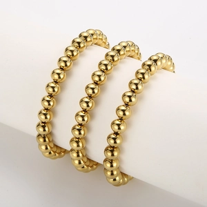Macro detail of three elastic gold bead bracelets on a white cylindrical jewelry display