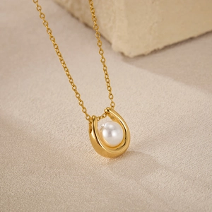 Close-up of a U-shaped gold horseshoe necklace featuring a round white pearl inlay