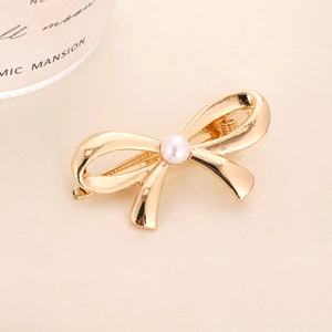 Elegant gold metal bow hair clip featuring a center pearl accent on a soft beige background