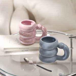 Detail of bubble-shaped ceramic mugs in pearl pink and blue on a glass table