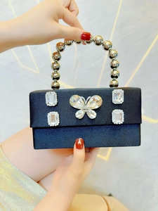 Close-up of black satin evening bag featuring rhinestone butterfly and silver bead handle