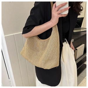 Close-up of a khaki woven tote bag worn on the shoulder in a minimalist setting