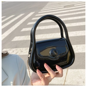 Detail of a black glossy patent leather mini bag with an elegant gold chain strap