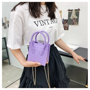 Detail of purple crocodile pattern handbag with gold chain strap held by a model