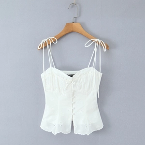 Detail of white cotton top featuring floral embroidery, adjustable ties and buttons