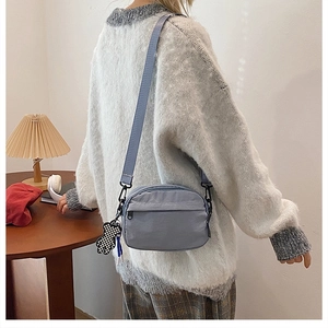 Détail du sac bandoulière en nylon bleu-gris avec boucle en métal et pendentif d'ours