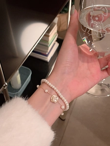 Primer plano de pulsera de perlas de doble capa con colgante de camelia dorada