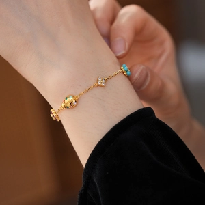 Detail of gold bracelet featuring ladybug and clover charms with colorful inlaid gems