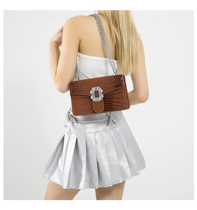 Detail of brown crocodile embossed crossbody bag with sparkling rhinestone buckle and chain