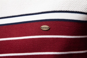 Detail of striped knit sweater showing texture and metal emblem on chest area