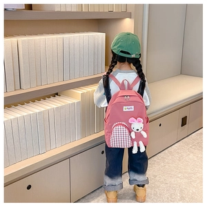 Pink cartoon kids backpack with red plaid pocket and plush bunny on a library background