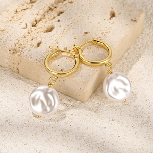 Macro shot of elegant baroque pearl earrings with golden hoops on a stone background