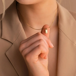 Macro shot of gold square pendant necklace with engraved letter R on a female model