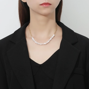 Close-up of a half baroque pearl and half gold paperclip chain necklace on a model