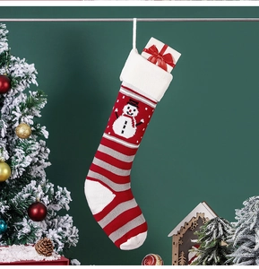 Knitted Christmas stocking with snowman pattern hanging on green wall background