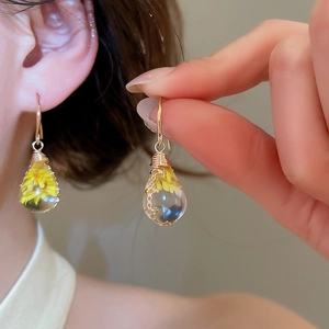 Detailed view of handmade resin drop earrings featuring delicate yellow dried flowers