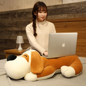 Plush dog toy used as a laptop stand on a bed, showing its large size and functional use