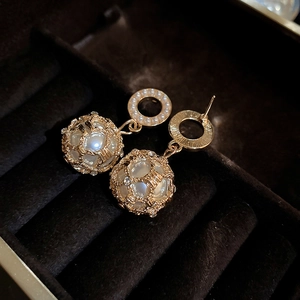 Detail of gold hollow metal mesh earrings with faux pearls on black velvet jewelry box